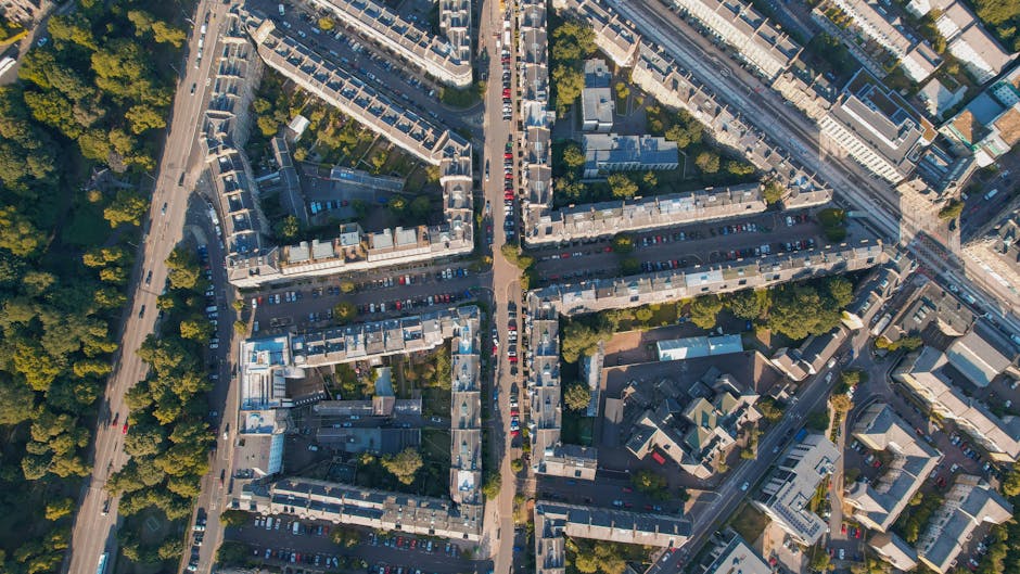 An aerial view capturing a residential neighbourhood with tightly packed terraced houses arranged in a grid-like pattern, some with small backyards and trees lining the streets. The image shows a dayt