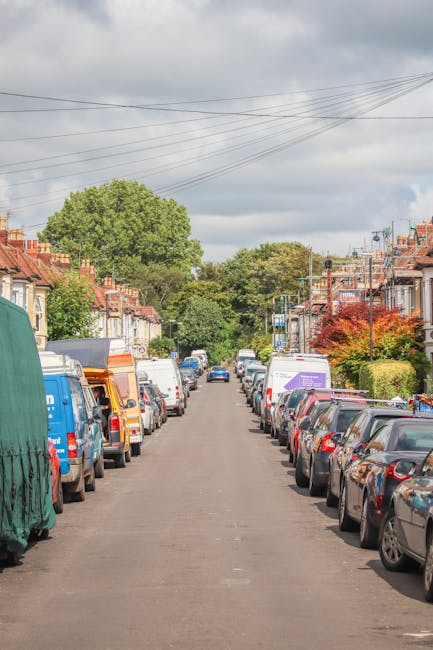 A city street scene in Haringey featuring a partially visible red double-decker bus approaching from the background, with several parked cars lined along the curb on both sides of the road. In the for